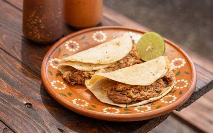 Dos tacos blandos de birria en tortilla de maíz, servidos con limón